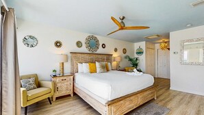 Un dormitorio con cama de madera, una silla, una mesita de noche, un ventilador de techo y adornos en la pared.