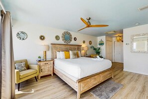 A bedroom with a wooden bed, a chair, a nightstand, a ceiling fan, and wall decorations. - Oceanfront Largo Mar Home w/ a Private Balcony plus Free WiFi & Beach Access (Panama City Beach)