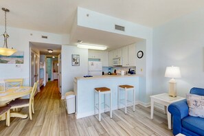 A modern kitchen with white cabinets, a microwave, and a sink. There is a dining area with a table and chairs, and a blue sofa with a lamp. - Gorgeous condo with private balcony, shared pool & beach access (Panama City)