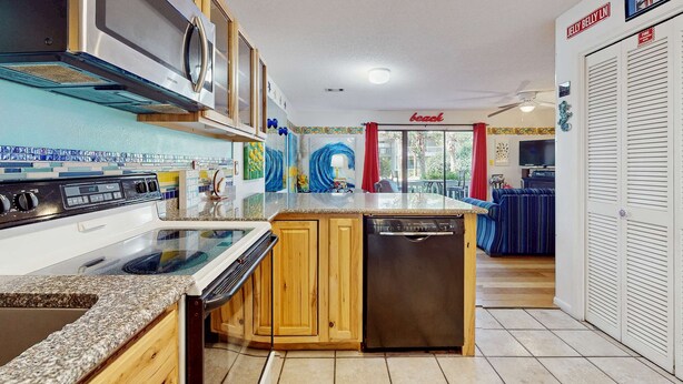 A kitchen with a stove, microwave, and dishwasher. There is a dining area with a blue-striped sofa and a red curtain. - Cute ground floor condo with shared pool, access to shuffleboard and tennis (Santa Rosa Beach)