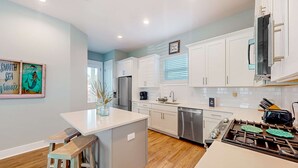 Una cocina moderna con armarios blancos, una isla central, un refrigerador de acero inoxidable y una estufa a gas.