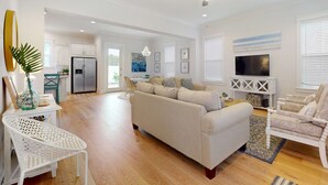 Un amplio salón con un sofá beige, un sillón blanco y una zona de comedor con mesa y sillas.