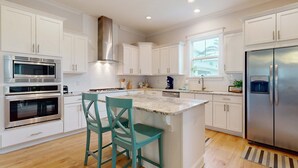 Una cocina moderna con armarios blancos, electrodomésticos de acero inoxidable y una isla central con dos sillas.