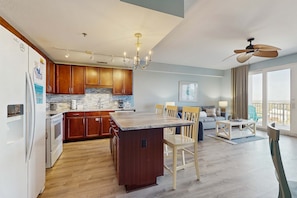 A modern kitchen with wooden cabinets, a central island, and a dining area with chairs and a table. - Beachview Condo with full kitchen, shared pool and beach access (Panama City Beach)