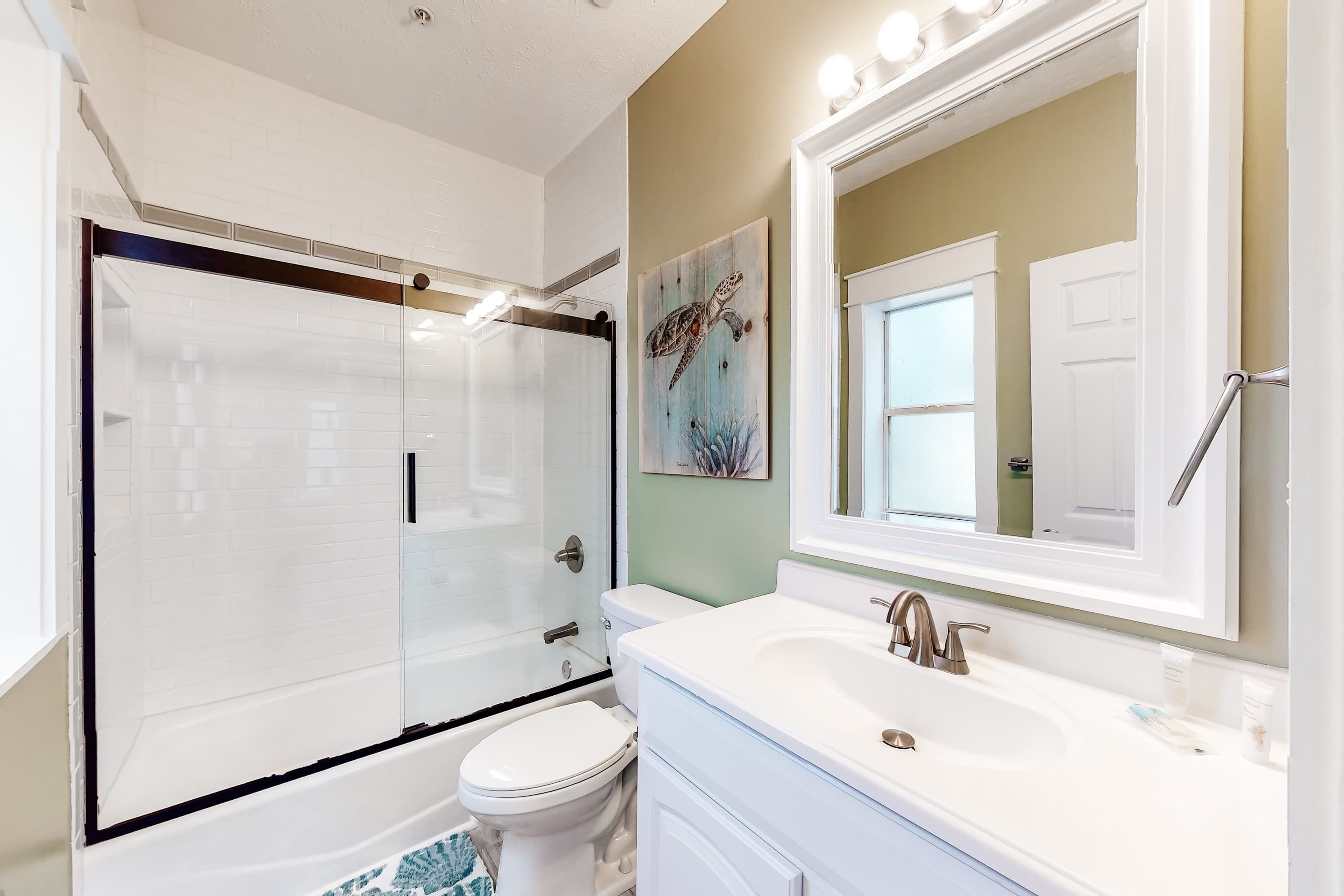 A bathroom with a glass shower enclosure, a white toilet, a white sink, and a large mirror.