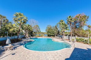 A swimming pool with a curved edge, surrounded by lounge chairs and umbrellas, with palm trees and a clear blue sky in the background. - New Cottage Near 30A Rosemary Beach with 2 Master Suites (Inlet Beach)