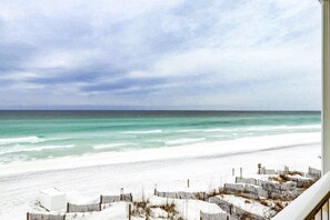 Une vue sur la plage, avec une rive de sable blanc, une clôture en bois et un bâtiment au premier plan.
