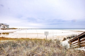 Vista de playa con un cartel, arena y un edificio al fondo.