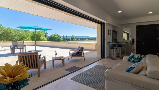 A spacious living area with a sofa, chairs, and a dining table. There is a large window offering a view of greenery and hills. - THE INTIMACY OF A PROVENCE ESTATE LA SUITE EUCALYPTUS 5 EPIS (Mollégès)