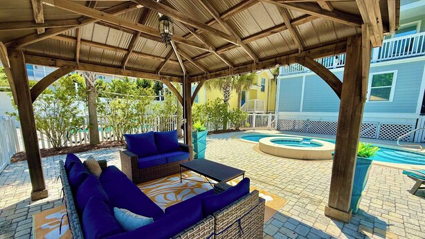 A covered outdoor seating area with wicker furniture and a pool. - Luxury home with private saltwater pool, spa, gazebo & deck - walk to beach (Santa Rosa Beach)