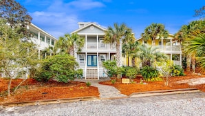 A two-story building with a porch, surrounded by palm trees and a well-maintained garden. - Luxury home with private saltwater pool, spa, gazebo & deck - walk to beach (Santa Rosa Beach)