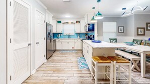 A modern kitchen with white cabinets, a central island, and a dining area with a white table and chairs. - Luxury home with private saltwater pool, spa, gazebo & deck - walk to beach (Santa Rosa Beach)
