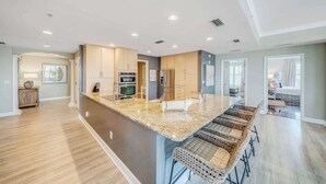 A modern kitchen with a central island, built-in appliances, and a seating area with wicker chairs. - Luxurious bayfront condo in a gated resort with an amazing pool & hot tub (Panama City Beach)