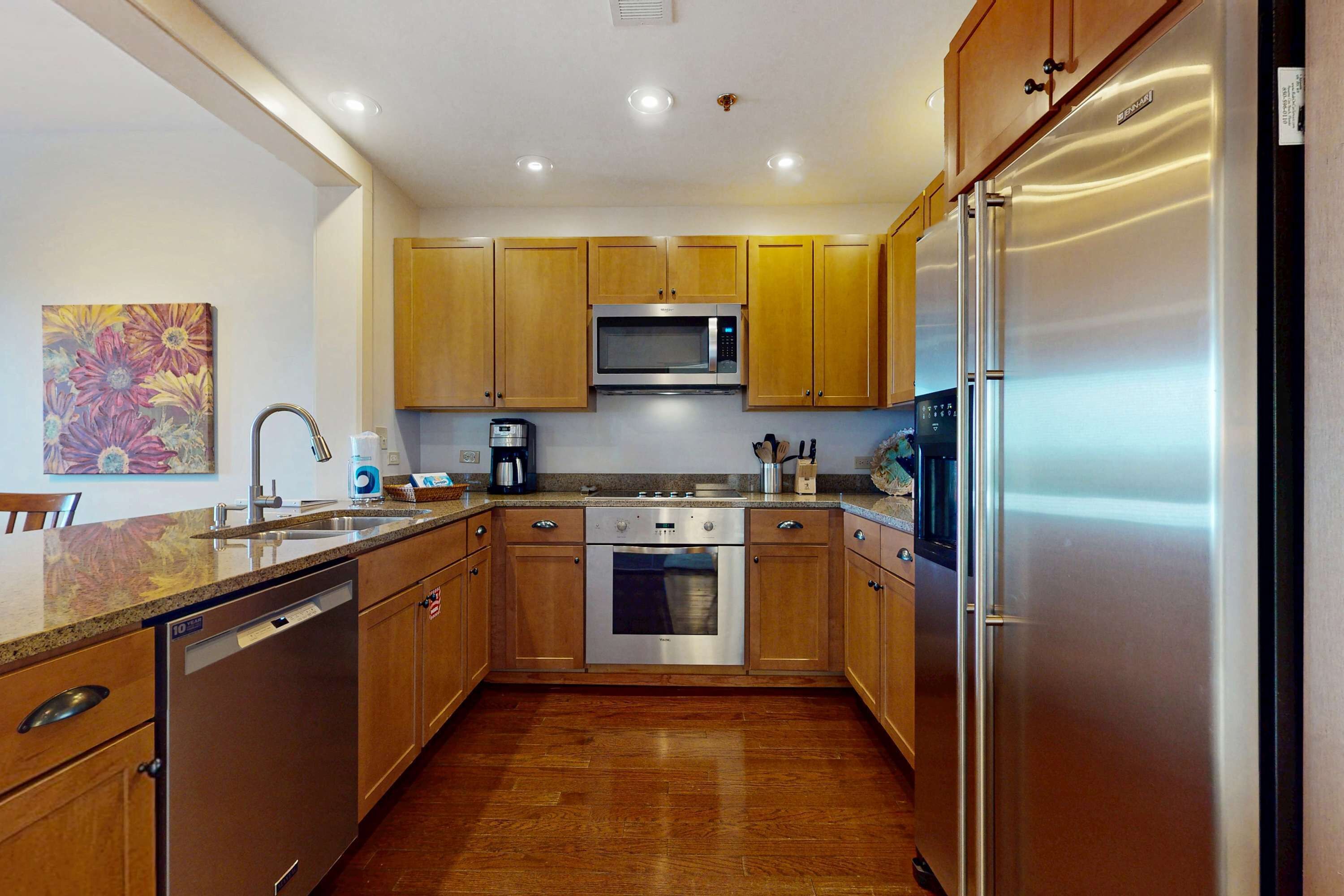 A kitchen with wooden cabinets, stainless steel appliances, and a wooden floor.