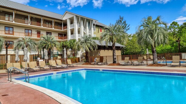 A hotel with a swimming pool, multiple balconies, and palm trees. - Polished condo with balcony & pools - one block from the beach (Santa Rosa Beach)