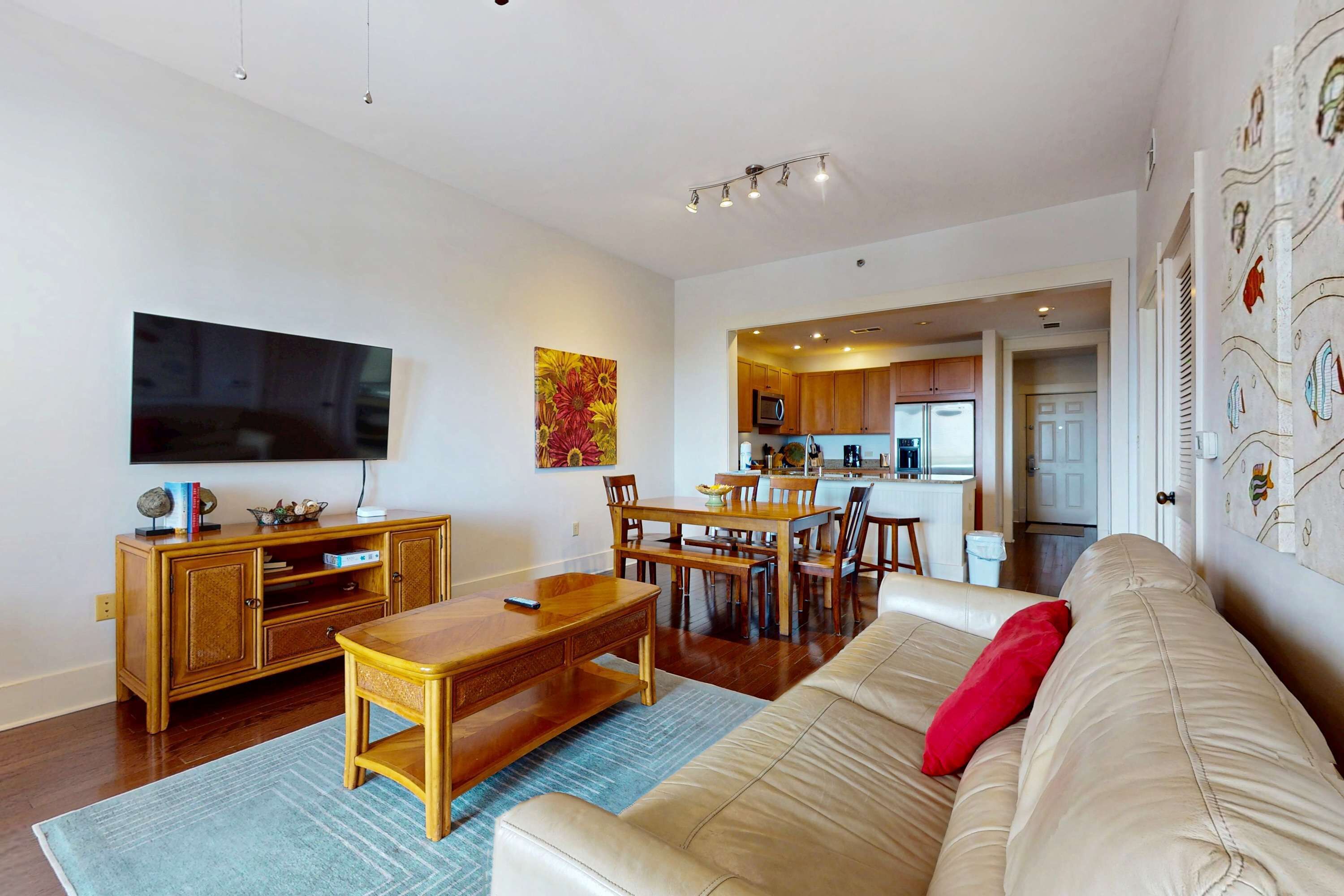 Een moderne woonkamer met een flatscreen televisie, houten meubels en een keuken op de achtergrond.