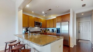 A modern kitchen with wooden cabinets, stainless steel appliances, and a granite countertop. - Polished condo with balcony & pools - one block from the beach (Santa Rosa Beach)