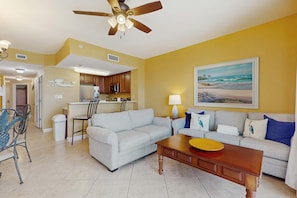 A living room with a ceiling fan, a dining area with chairs, a kitchen with cabinets, and a painting on the wall. - Gulf Front Family friendly getaway with Beach Service (Panama City Beach)