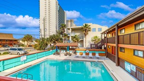 A swimming pool with lounge chairs and umbrellas, surrounded by buildings and palm trees. - Lovely second-floor condo w/beach access & shared outdoor pool (Panama City Beach)