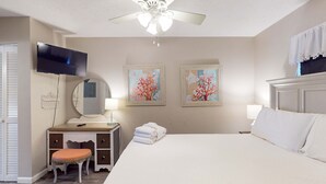 A bedroom with a bed, a vanity with a mirror, a ceiling fan, and two wall-mounted paintings. - Lovely second-floor condo w/beach access & shared outdoor pool (Panama City Beach)