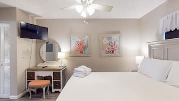 Quarto com cama, penteadeira com espelho, ventoinha no teto e duas pinturas penduradas na parede.