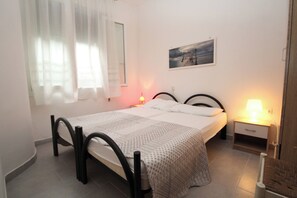 A bedroom with a bed, two bedside tables, a nightstand, a window with sheer curtains, and a wall-mounted picture. - Welcoming Apartment for Families in Rosolina Mare (Rosolina)