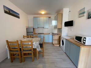 A compact kitchen with a dining table, chairs, a microwave, and a washing machine. - Welcoming Apartment for Families in Rosolina Mare (Rosolina)