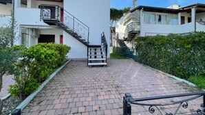 Ein Wohngebäude mit einer Treppe, die zu einem Balkon führt, umgeben von Grünpflanzen und gepflasterten Wegen.