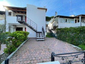 A residential building with a staircase leading to a balcony, surrounded by greenery and paved walkways. - Welcoming Apartment for Families in Rosolina Mare (Rosolina)