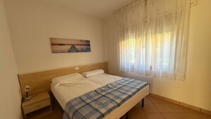 A bedroom with a bed, a nightstand, a lamp, a painting on the wall, and a window with curtains. - Cozy Flat With Private Parking in Rosolina Mare (Rosolina)