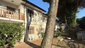A two-story building with a balcony, a bicycle, and a tree in the yard. - Cozy Flat With Private Parking in Rosolina Mare (Rosolina)