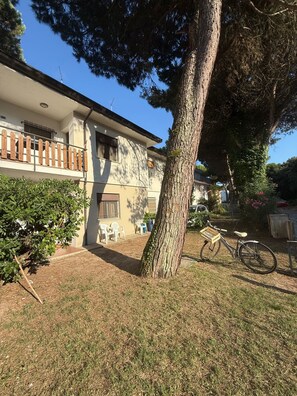 A two-story building with a balcony, a bicycle, and a tree in the yard. - Cozy Flat With Private Parking in Rosolina Mare (Rosolina)