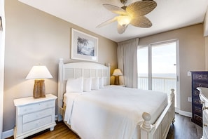 A bedroom with a large bed, two bedside tables with lamps, a ceiling fan, a window with curtains, and a framed picture on the wall. - Cool & contemporary beachfront getaway with large balcony, pools, & gym (Panama City Beach)