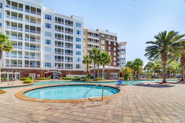A hotel with multiple floors, outdoor swimming pools, and palm trees. - Snowbird-friendly condo with waterfront view, WiFi, AC, access to pool, hot tub (Panama City Beach)