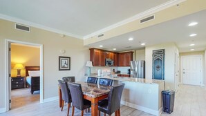 A spacious kitchen with a dining area, featuring a marble-top table and chairs, wooden cabinets, and a built-in microwave. - Snowbird-friendly condo with waterfront view, WiFi, AC, access to pool, hot tub (Panama City Beach)