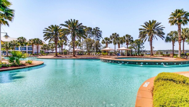 A clear swimming pool with palm trees and lounge chairs around it. - Snowbird-friendly condo with waterfront view, WiFi, AC, access to pool, hot tub (Panama City Beach)