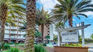 A hotel sign with "Reflections Serenity Spa" and "Full Service Spa & Salon" written on it, surrounded by palm trees and a multi-story building in the background. - Snowbird-friendly condo with waterfront view, WiFi, AC, access to pool, hot tub (Panama City Beach)