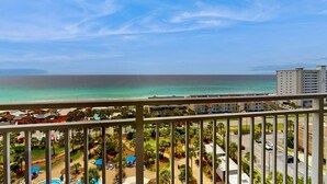 A balcony with a view of a beach, a pool, and a resort area. - Gulf front penthouse w shared pools, snack shack, community grill & more (Destin)