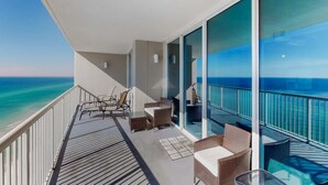 A balcony with wicker furniture, a glass door leading to a pool, and a view of the ocean. - Bright Gulf-facing condo on the beach with pool & hot tub (Panama City Beach)