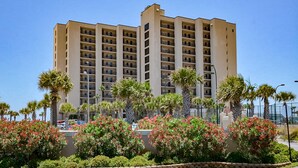 A multi-story hotel with a uniform facade, surrounded by palm trees and flowering shrubs. - Spacious fourth-floor condo - Complimentary BEACH SERVICE (Navarre Beach)