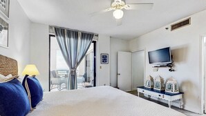 A hotel room with a large bed, a ceiling fan, a television mounted on the wall, and a small table with decorative items. - Spacious fourth-floor condo - Complimentary BEACH SERVICE (Navarre Beach)
