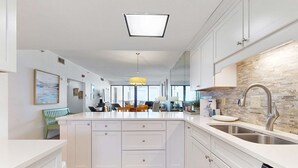A modern kitchen with white cabinetry, a central island, a large window, and a pendant light. - Spacious fourth-floor condo - Complimentary BEACH SERVICE (Navarre Beach)