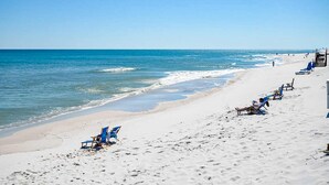 A beach with rows of blue beach chairs and umbrellas, a sandy shore, and the ocean. - Spacious fourth-floor condo - Complimentary BEACH SERVICE (Navarre Beach)
