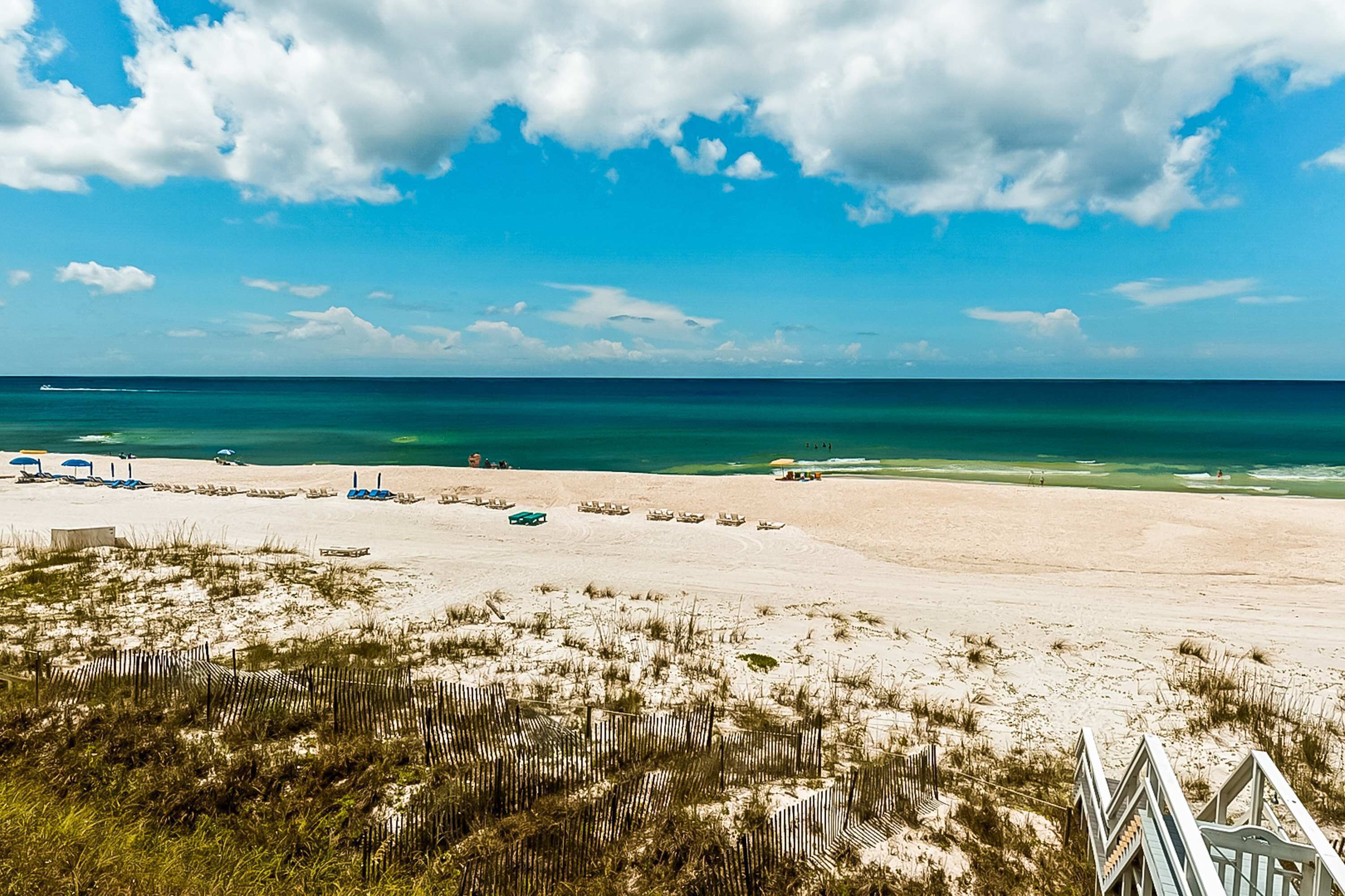 Une plage avec une clôture en bois, des chaises de plage et des parasols.