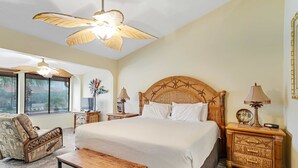 A bedroom with a large bed, a wooden nightstand, a chair, a bench, and a ceiling fan. - Conveniently located condo with shared pool & tennis, on-site golf - walk to beach (Panama City Beach)