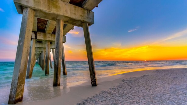 A pier extending into the ocean with a sunset in the background. - Light-filled beachfront condo with shared pool, hot tub & beach access (Panama City Beach)