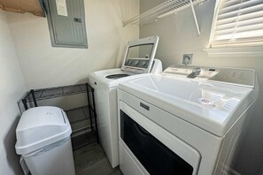 Ein kleiner Hauswirtschaftsraum mit einer Frontlader-Waschmaschine und einem Trockner, einem Wäscheständer aus Metall und einem Mülleimer.