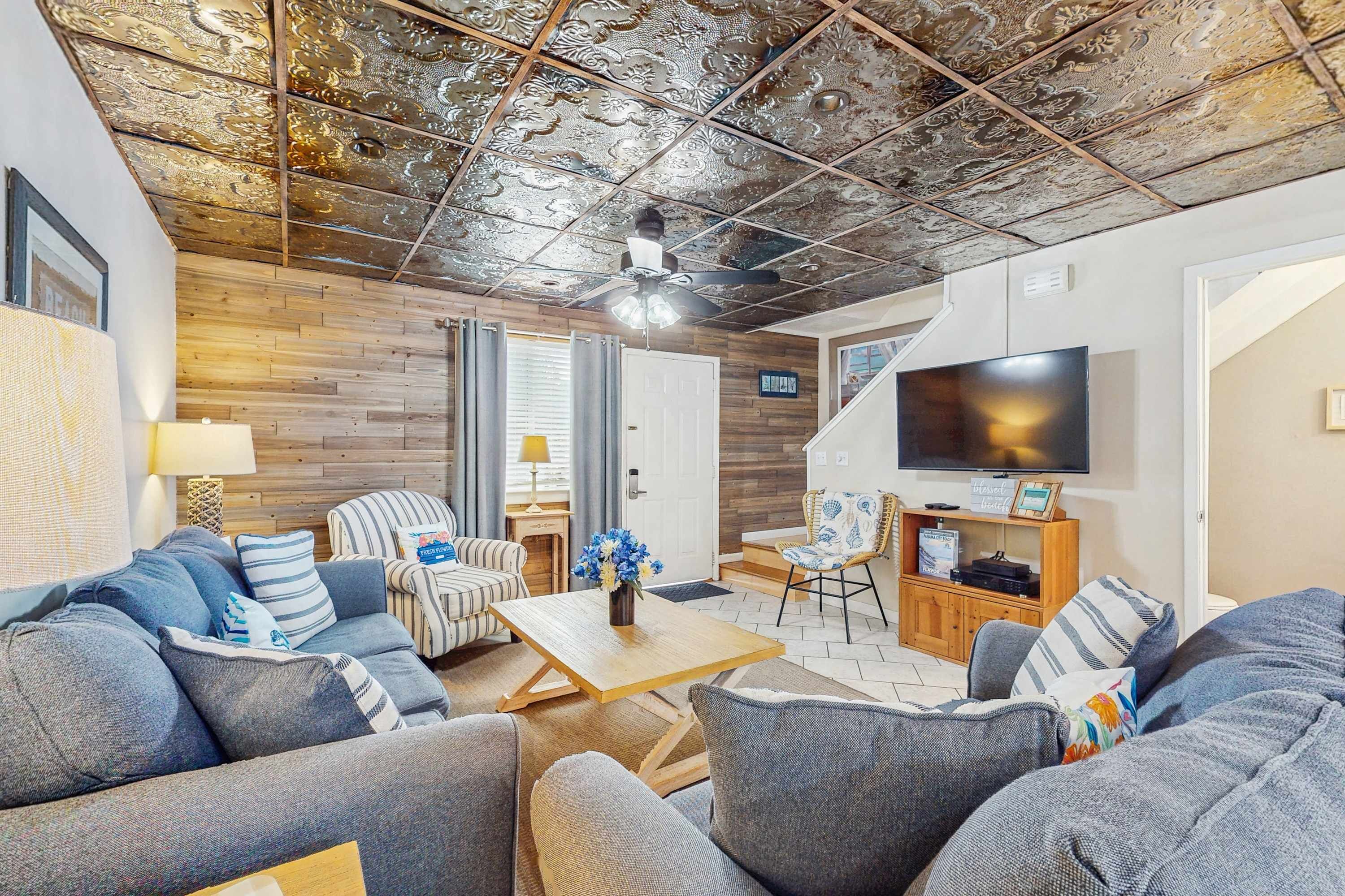 A modern living room with a wooden ceiling, a flat-screen TV, and a sofa set.