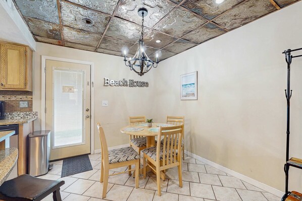 A dining area with a wooden table and chairs, a chandelier, and a sign reading "Beach House". - Stunning sunlit townhome with pool, balcony, & AC - near beaches & boardwalks (Panama City Beach)