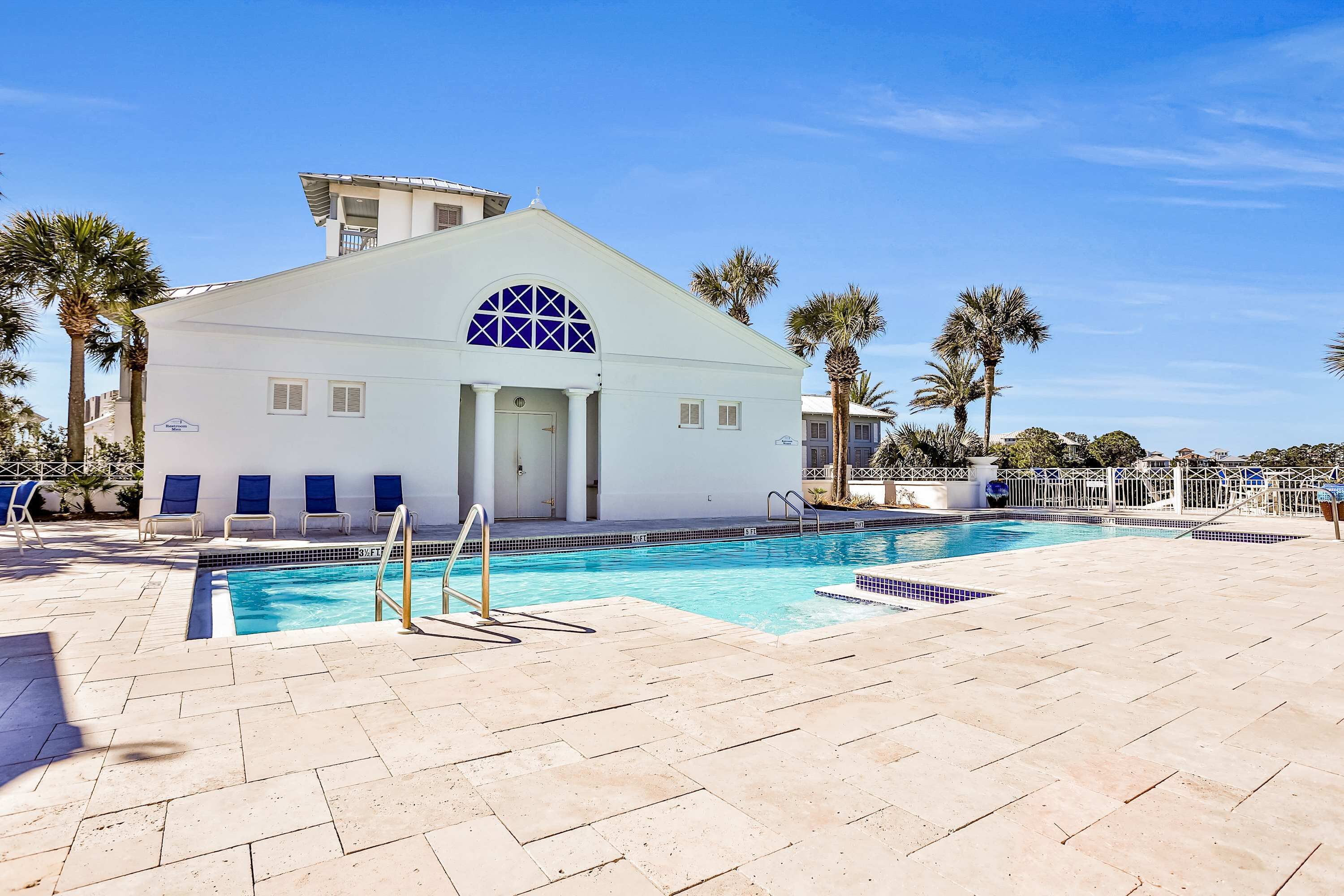 A pool area with a white building, palm trees, and a clear blue sky.